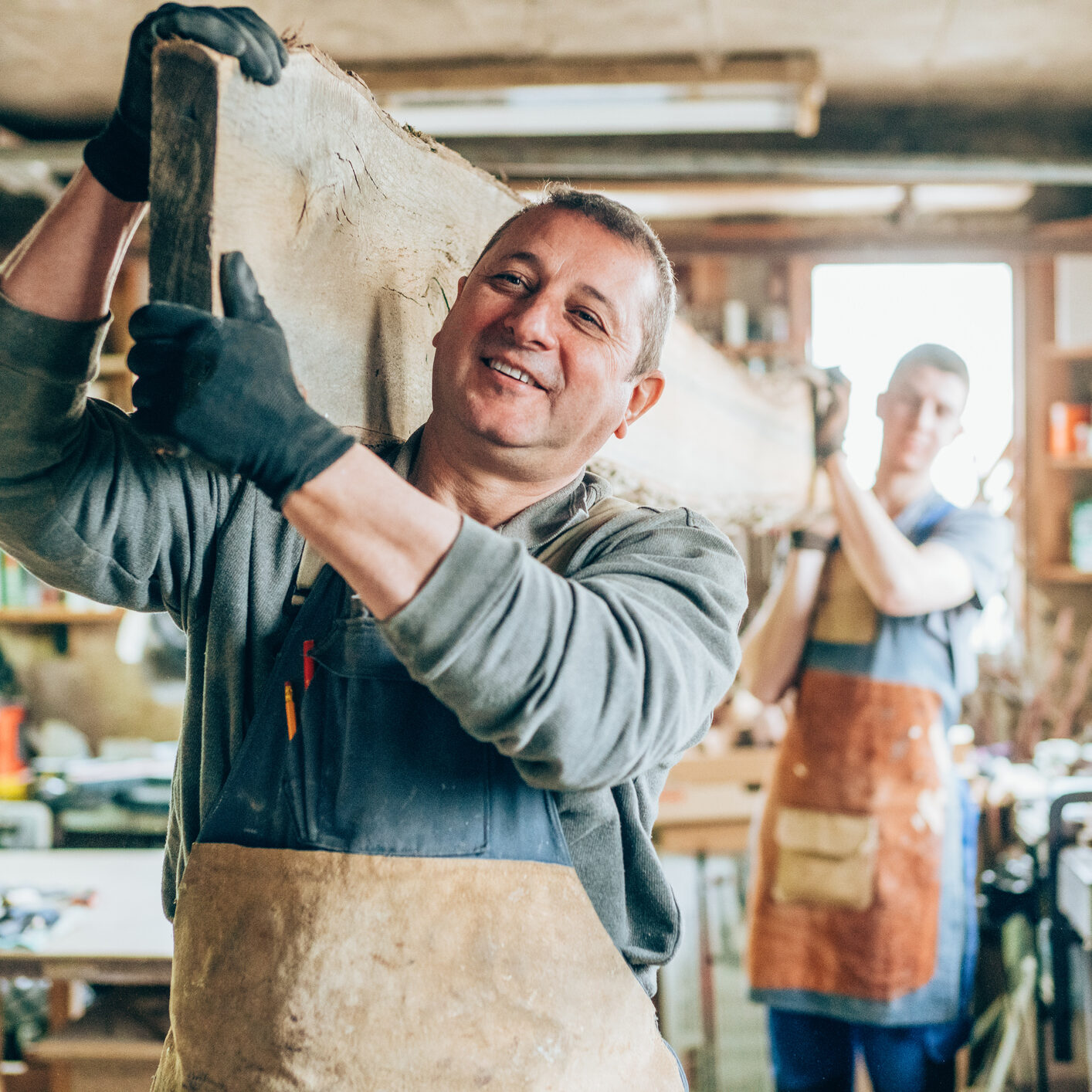 Father and son carpenters carrying a wood plank in their wood workshop